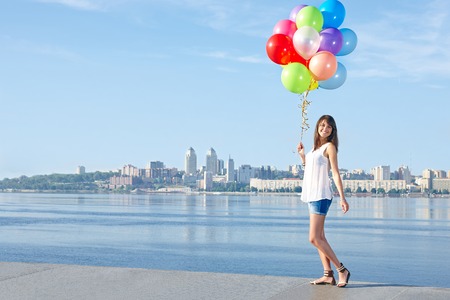 Happy young woman with colorful balloons in full length, urban sceneの写真素材
