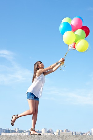 Happy young woman flying away with colorful balloons in full length, urban scene,city view, outdoorsの写真素材