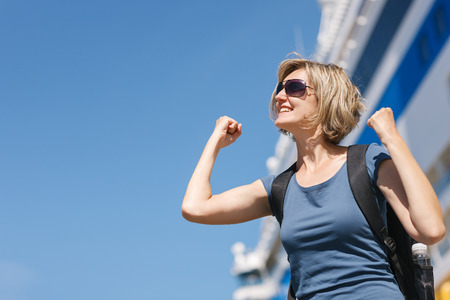 Happy excited woman tourist screaming of joy with hands raised, in front of big cruise liner, summer dayの写真素材