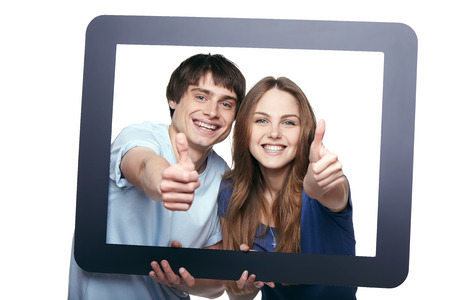 Happy couple looking through tablet frame and giving thumbs upの写真素材