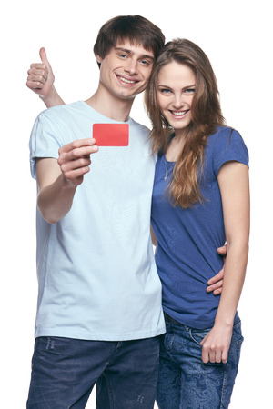 Happy couple in tshirts hugging, man showing blank credit card, woman gesturing thumb up, on white backgroundの写真素材