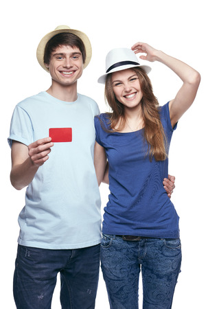 Happy couple in tshirts and straw hats hugging, man showing blank credit card, on white backgroundの写真素材
