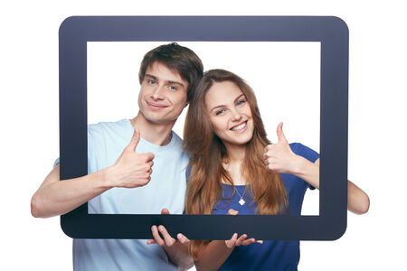 Happy couple looking through tablet frame and giving thumbs upの写真素材