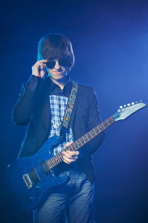 Young guitarist on stage standing in smoke lowering his sunglassesの写真素材