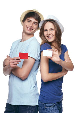 Happy couple in tshirts and straw hats standing back to back, showing blank credit cards, on white backgroundの写真素材
