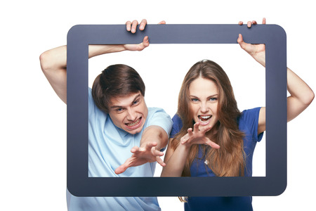 Funny picture of young couple going to grasp you through tablet frame, over white backgroundの写真素材
