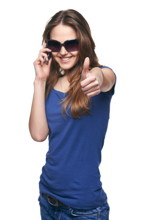 Smiling young woman in sunglasses gesturing thumb up while talking on cell phone. Selective focus, focus on thumb.の写真素材