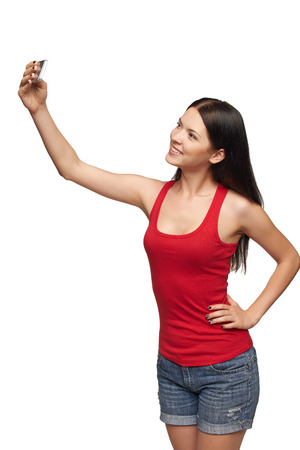 Happy young girl taking pictures of herself through cellphone, over white backgroundの写真素材