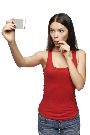 Happy surprised young girl taking pictures of herself through cellphone, over white backgroundの写真素材