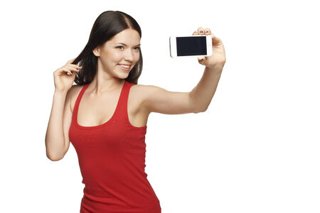 Happy flirting young girl taking pictures of herself through cell phone, over white backgroundの写真素材