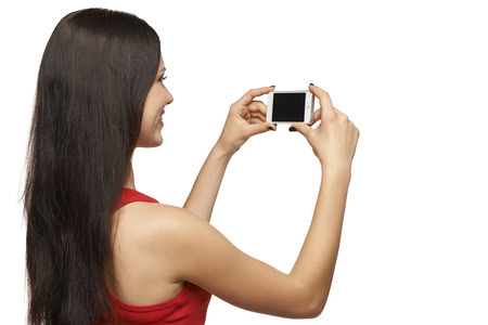 Happy young girl taking pictures of herself through cell phone, over white backgroundの写真素材