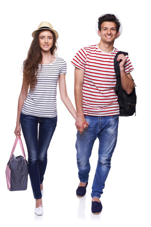Full length of young happy couple walking with travel bags with joined hands, isolated on white backgroundの写真素材