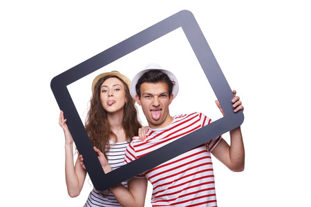 Young couple having fun making faces and showing tongue through tablet frameの写真素材