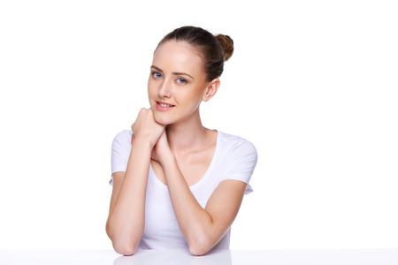 Beauty girl portrait  Young natural woman with clean face sitting at white table leaning on her elbows, over white backgroundの写真素材