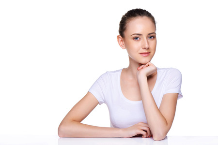 Beauty girl portrait  Young natural woman with clean face sitting at white table leaning on her elbows, over white backgroundの写真素材