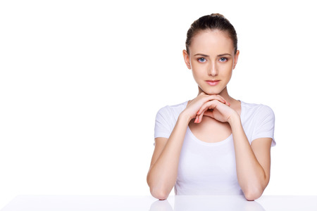 Beauty girl portrait  Young natural woman with clean face sitting at white table leaning on her elbows, over white backgroundの写真素材