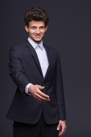 Smiling handsome business man with hand extended to handshake, over gray background  Focus on the hand の写真素材