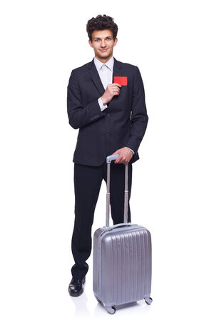 Full length of a businessman standing with a luggage, showing blank credit card, over white backgroundの写真素材