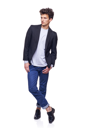Full body of a fashion man with modern haircut posing standing with crossed legs, looking away thoughtful, over white の写真素材