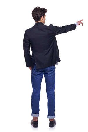 Full length back view of young trendy man pointing to the side on blank copy space, over white の写真素材