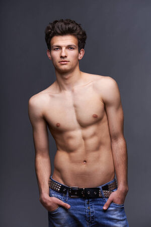 Male fashion model with modern haircut posing shirtless over dark backgroundの写真素材