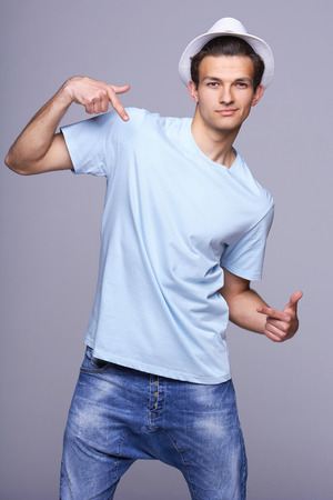 Fashion man wearing tshirt and fedora hat pointing at himselfの写真素材