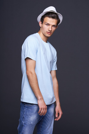 Man fashion model, stylish young man standing posing with hat, over black の写真素材
