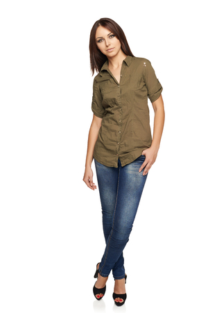 Young confident woman in jeans and green shirt standing relaxed in full length, over white studio backgroundの写真素材