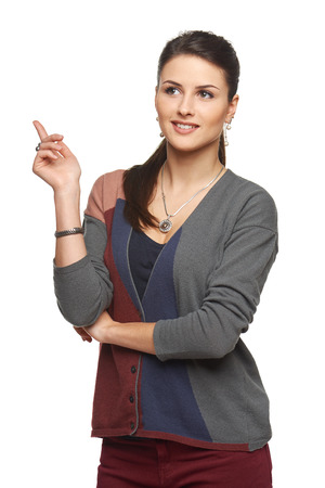 Smiling young woman in cardigan pointing at blank copy space, looking away, over white backgroundの写真素材