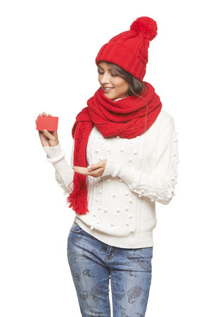 Winter, christmas, holidays concept. Smiling beautiful woman in red hat, scarf and mittens showing blank credit card over white backgroundの写真素材