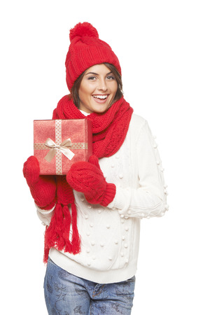 Christmas gift. Smiling beautiful woman in winter red hat and scarf holding red gift box, over white backgroundの写真素材