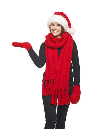 Smiling beautiful woman in Santa hat, scarf and mittens showing open hand palm with copy space for product or text, over gray backgroundの写真素材