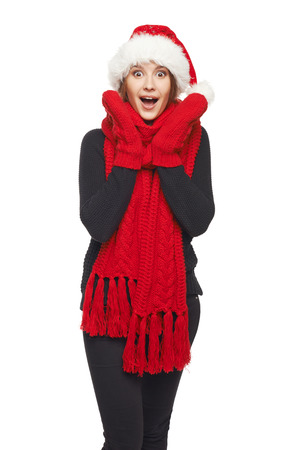 A beautiful happy surprised Christmas woman wearing santa hat and red scarf and mittens shouting of joy, over white backgroundの写真素材