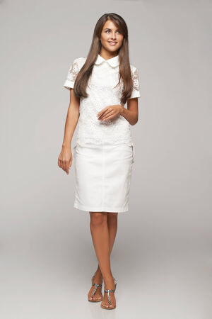 Portrait of smiling elegant business woman standing in full length looking away over gray backgroundの写真素材