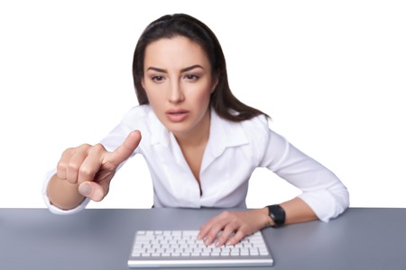 Portrait of a young business woman leaning against a keyboard and pointing at imaginary button, isolated on white. Shallow depth of field, focus on the finger.の写真素材