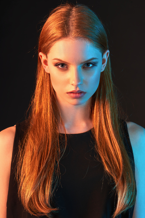 Fashion art portrait of beautiful red haired fashion model girl with long  hair in black dress over dark background, in colorful lightingの写真素材