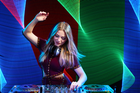 Beautiful DJ girl on decks at the party over colorful led backgroundの写真素材