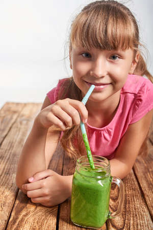Happy smiling little girl lying on wooden floor and drinking green smoothieの写真素材