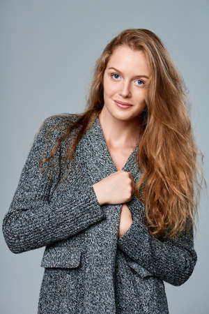 Happy smiling beautiful woman muffling in warm knitted cardigan, over gray backgroundの写真素材