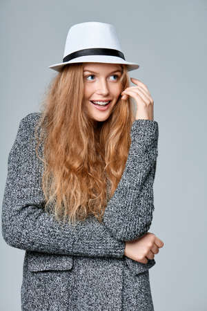 Playful smiling beautiful woman in warm knitted cardigan wloooking away at blank copy space, over gray backgroundの写真素材
