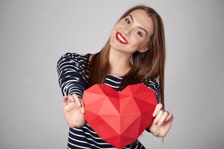 Smiling woman holding red polygonal paper heart shapeの写真素材