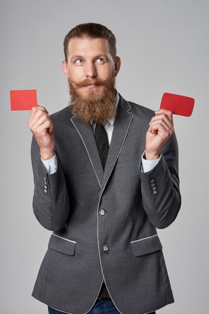 Hipster business man with beard and mustashes in suit standing over grey background showing two blank credit cards in every handの写真素材