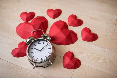 Closeup of big alarm clock with many red polygonal paper heart shapes over wooden bachgroundの写真素材