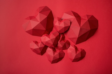 Heap of red polygonal paper heart shapes on red background, top viewの写真素材