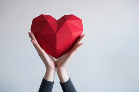 Two female hands holding red polygonal paper heart shapeの写真素材