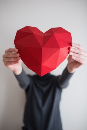 Woman outstretching red polygonal paper heart shape covering her face. Shallow depth of fieldの写真素材