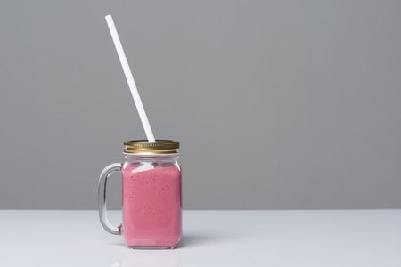 Jar tumbler mug with pink smoothie drink on tableの写真素材