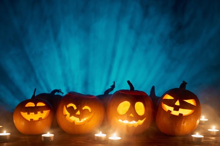Halloween pumpkins in a row with candles over blue light rays and smoke at background with copy space for text above, front viewの写真素材