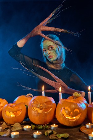 Halloween costume woman, tree girl, female with hands branches with burning pumpkins in front of her on smoky backgroundの写真素材