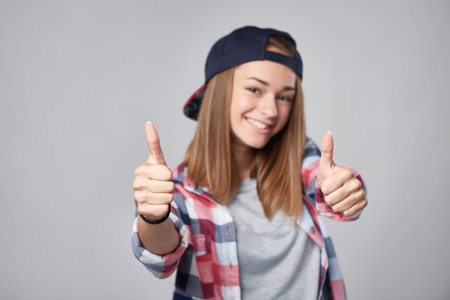 Emotional teen girl giving double thumb up over grey background. Closeup portrait, shallow depth of field, focus on handsの写真素材